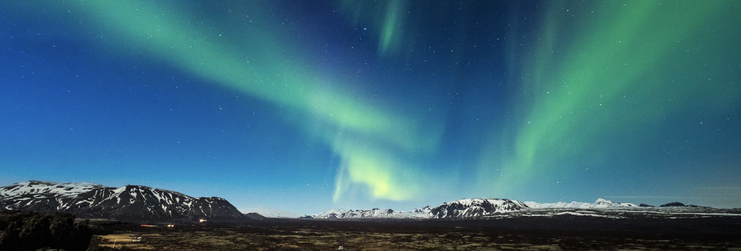 The aurora borealis glows green over snow-capped mountains in Iceland