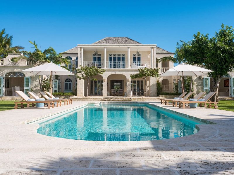 A two-story villa with a swimming pool, lounge chairs and umbrellas in the foreground