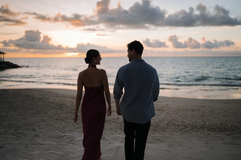 A couple walks along a beach at sunset